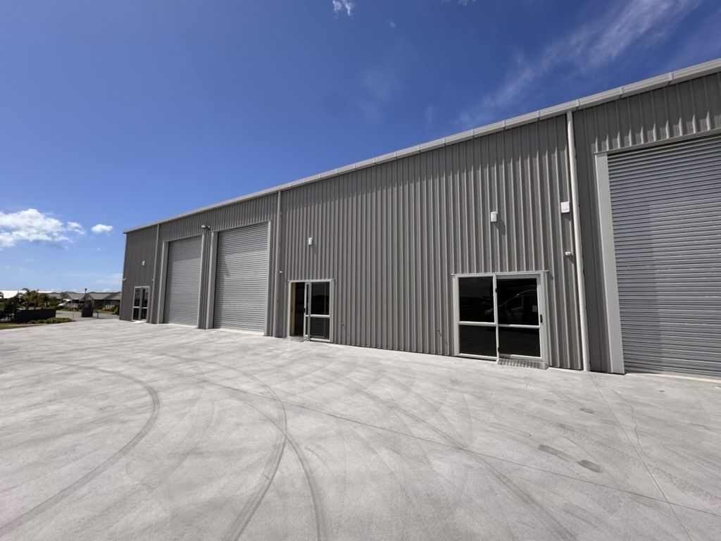 A new grey commercial building with three roller doors and a sealed yard under a blue sky